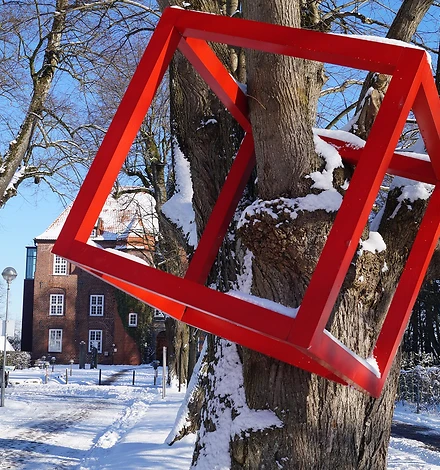 Ein roter Kubus hängt an einem Baum vor dem Hintergrund der verschneiten Schlossanlage.