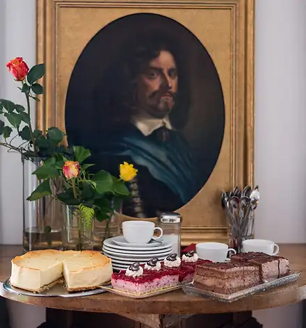 KunstKaffee&Kuchen Kuchen, Geschirr und Blumen vor einem Porträt in einem Goldrahmen.