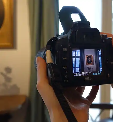Werkstatt für Kunst und Fotografie Hände halten eine Kamera. Auf dem Display und im Hintergrund sieht man ein Gemälde.