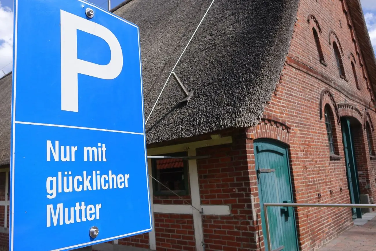 Blaues Parkplatzschild mit dem Hinweis: NUR MIT GLÜCKLICHER MUTTER