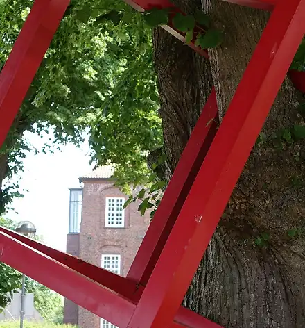 Kunstspaziergang zu den Skulpturen Ein roter Metallwürfel hängt an einem Baum.
