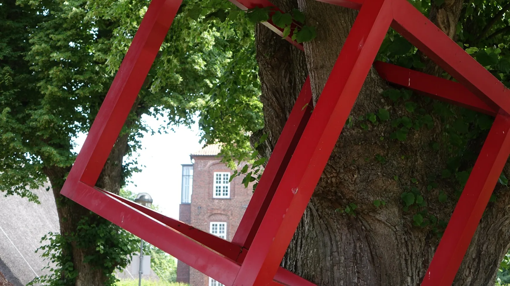 Ein roter Metallwürfel hängt an einem Baum.