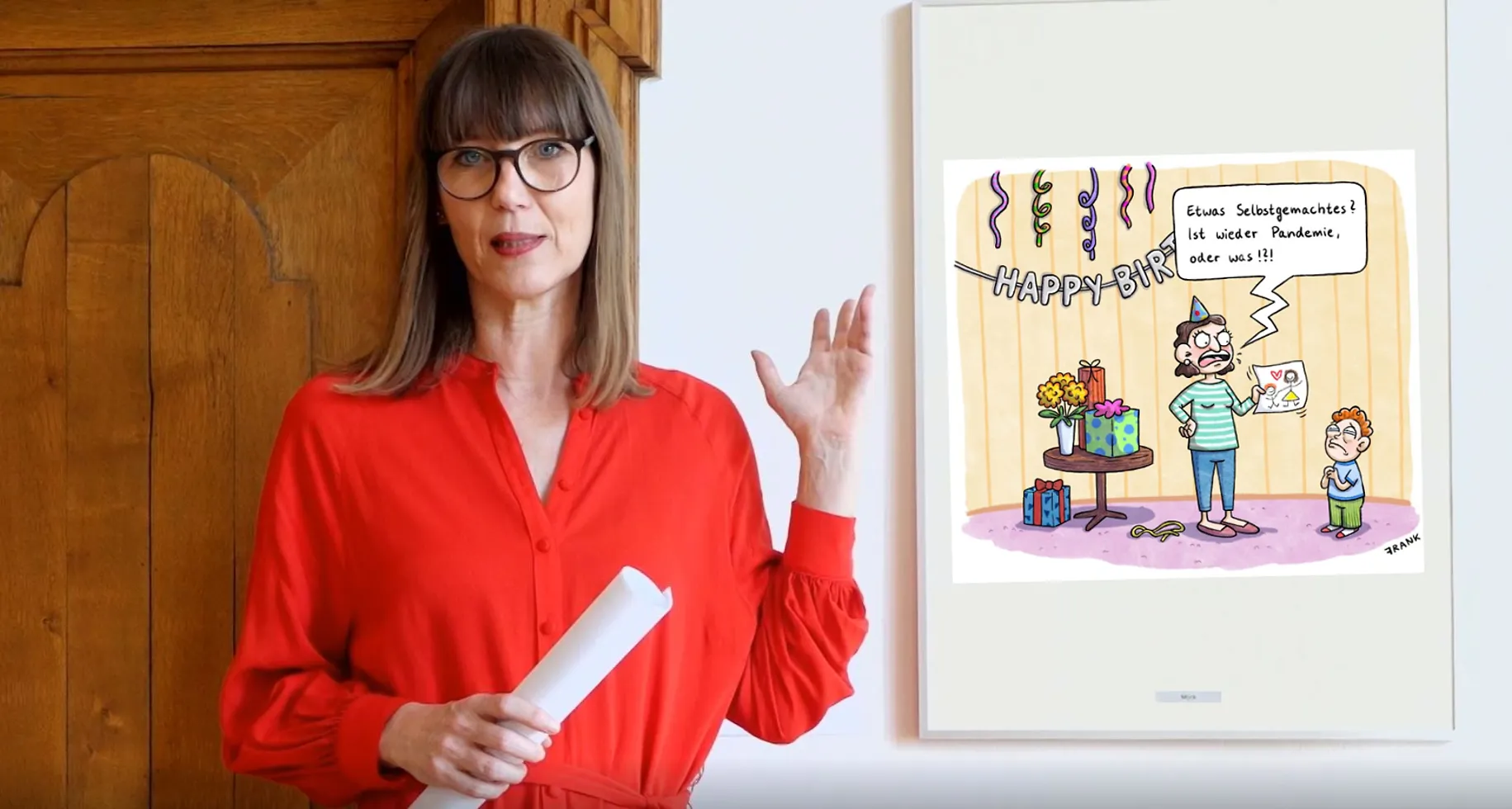 Claudia Rasztar zeigt auf eine gerahmte Karikatur.