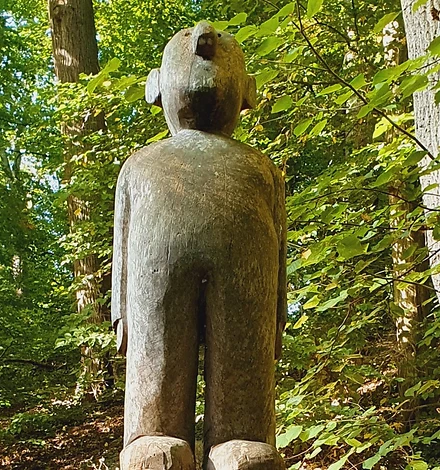 Eine aus Holz geschnitzte Figur eines Männchens steht mitten im Park.