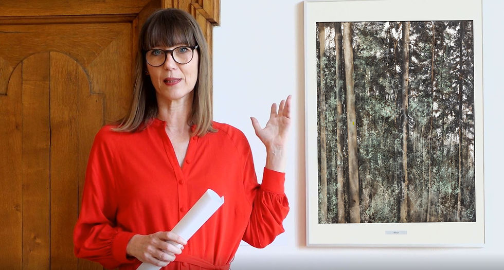 Claudia Rasztar zeigt auf ein Gemälde mit Bäumen.