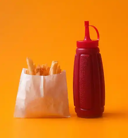 Food Truck am Festivalwochenende Eine Tüte Pommes und eine Flasche Ketchup vor orangenem Hintergrund.