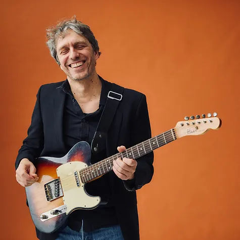 Foto von Lothar Müller mit Gitarre vor einem orangen Hintergrund