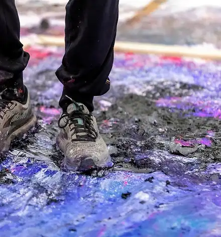 Performance mit Janus Hochgesand – High Intensity Painting Zwei Füße in Turnschuhen auf einer Leinwand voller Farbe.