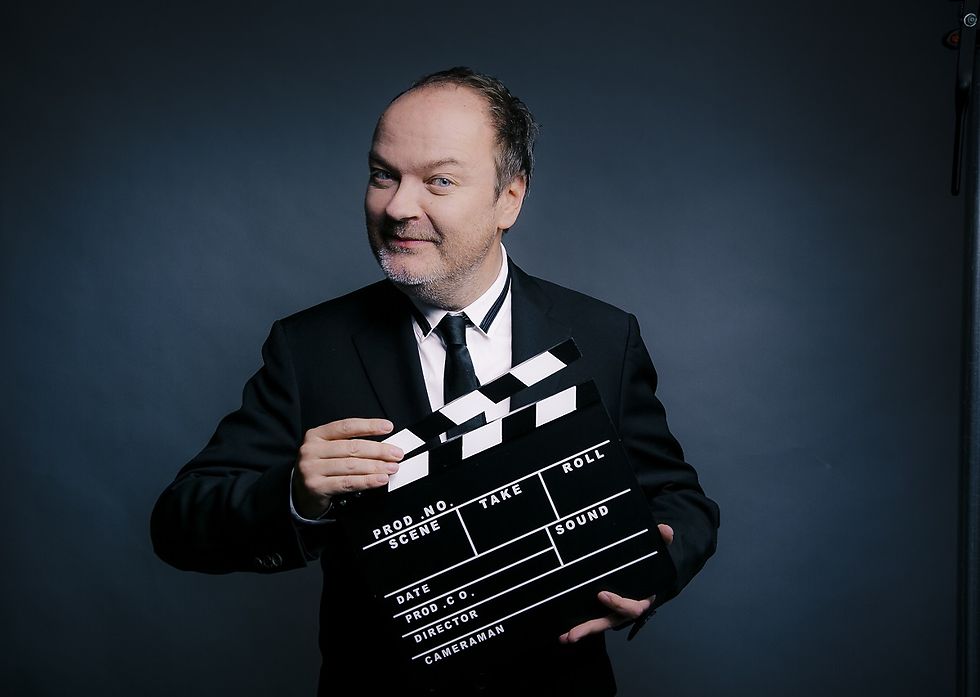 Jens Wawrczeck mit einer Filmklappe vor dunkelblauem Hintergrund.