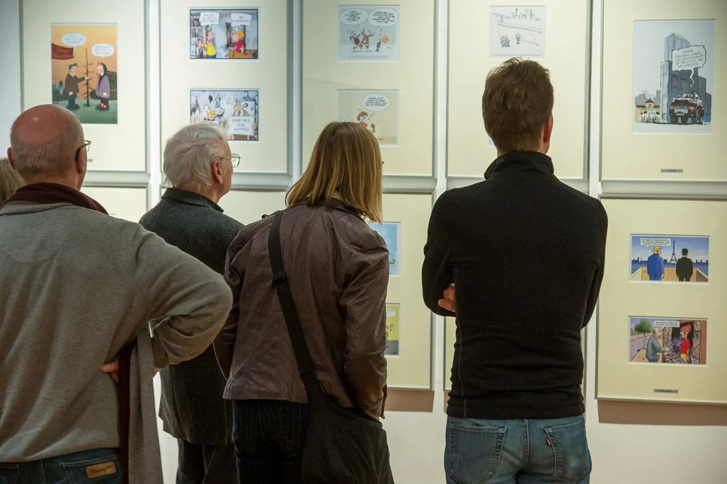 Eine Gruppe Besucherinnen und Besucher betrachtet gerahmte Karikaturen im Schloss.
