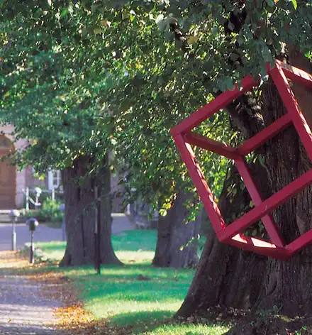 Kunstspaziergang zu den Skulpturen Ein roter Kubus aus Metall hängt in einem Baum vor dem Schloss.