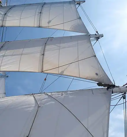 Eine Frau sitzt auf dem Mast eines großen Segelschiffs