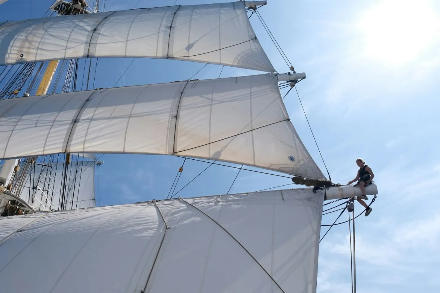 Eine Frau sitzt auf dem Mast eines großen Segelschiffs