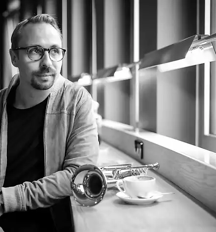 Menzel Mutzke Quartett - "Spring"-Tour Menzel Mutzke sitzt an einem Tisch und sieht aus dem Fenster. Auf dem Tisch ist seine Trompete und eine Tasse Kaffee.