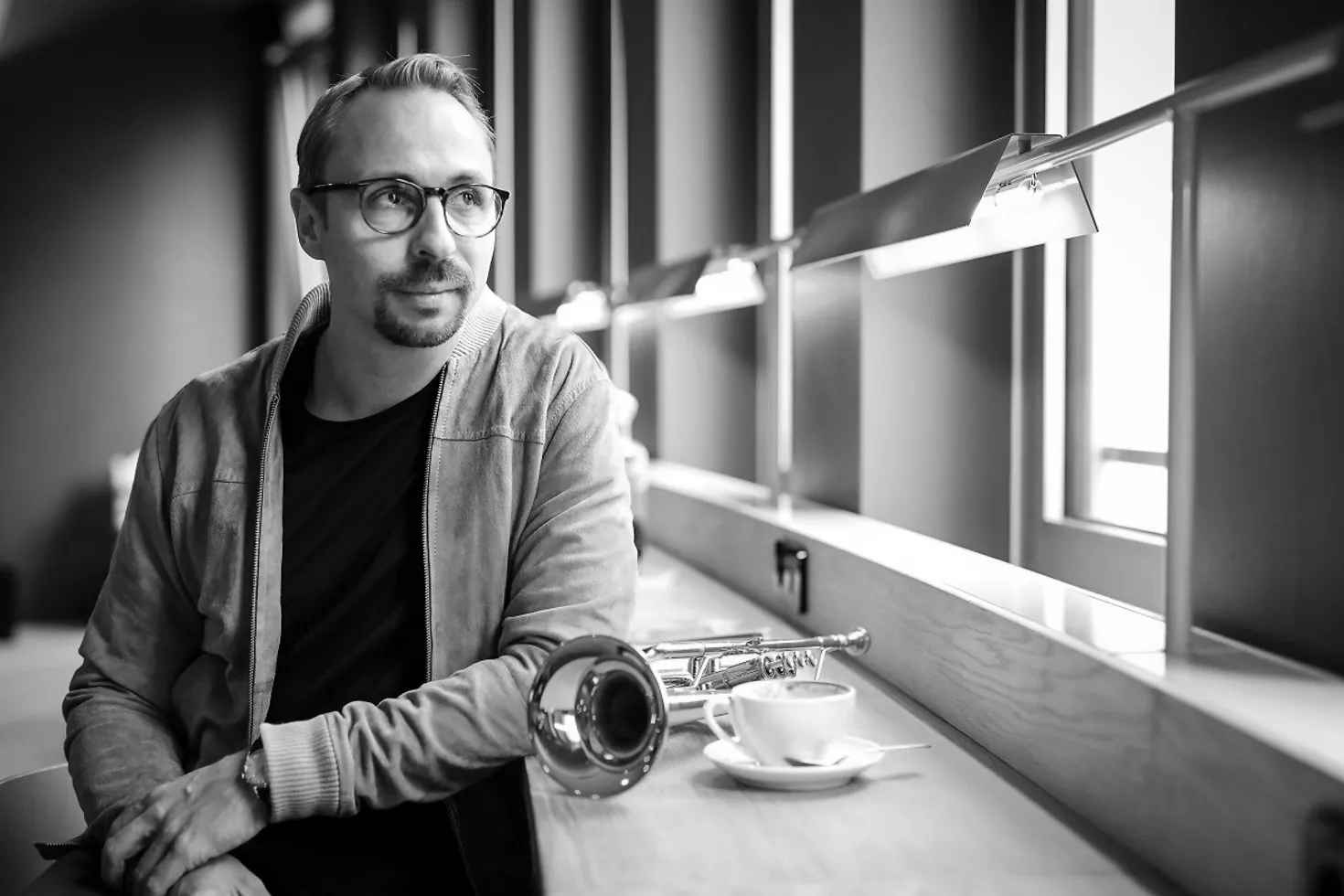 Menzel Mutzke sitzt an einem Tisch und sieht aus dem Fenster. Auf dem Tisch ist seine Trompete und eine Tasse Kaffee.