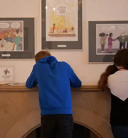 Ein Schüler und eine Schülerin zeichnen in der Karikaturenausstellung.