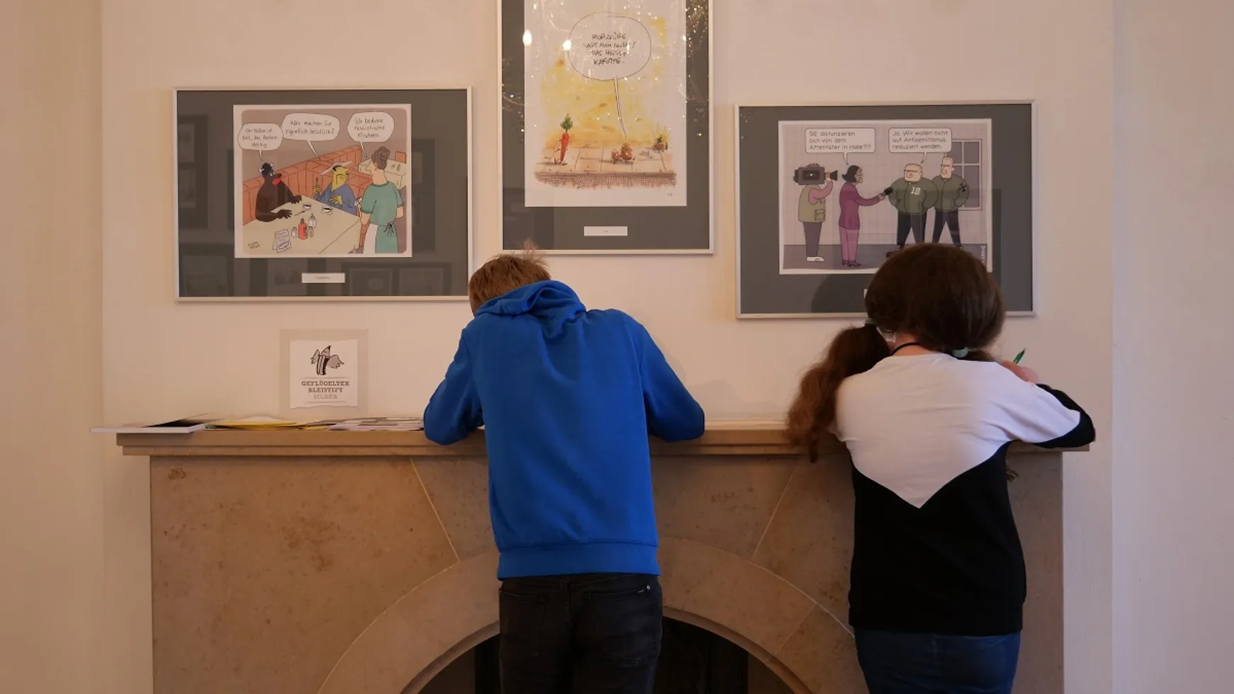 Ein Schüler und eine Schülerin zeichnen in der Karikaturenausstellung.