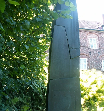 Eine Stele aus Bronze, im Hintergrund sieht man das Schloss.
