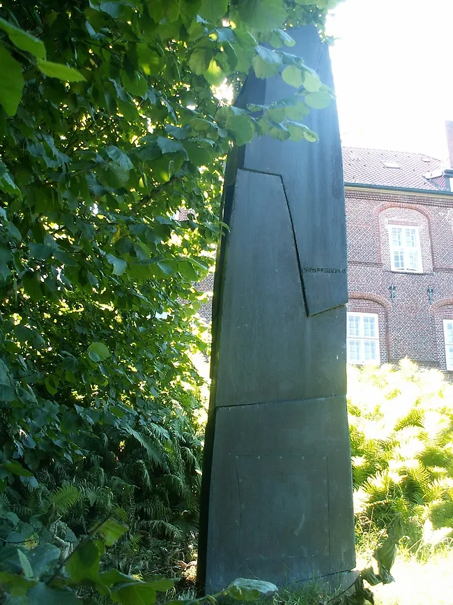 Eine Stele aus Bronze, im Hintergrund sieht man das Schloss.