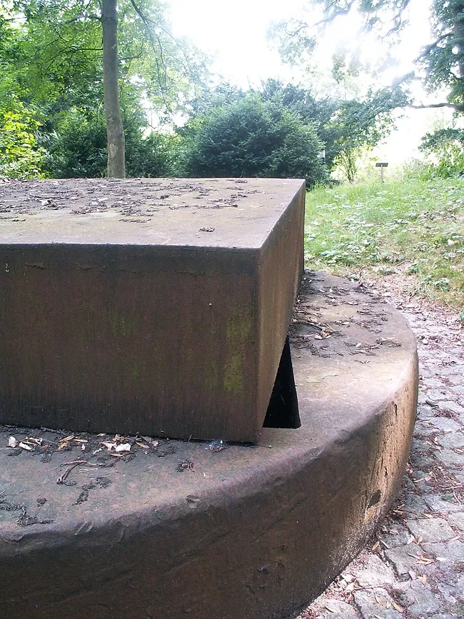 Foto der Skulptur, im Hintergrund sieht man das Grün des Parks.