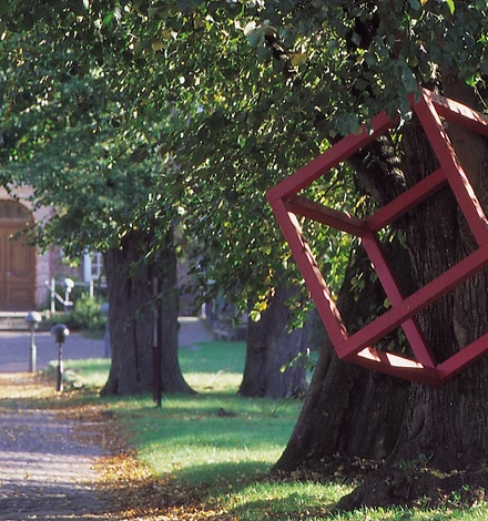 Ein großer roter Kubus aus Aluminium hängt in der Linde vor dem Schloss.