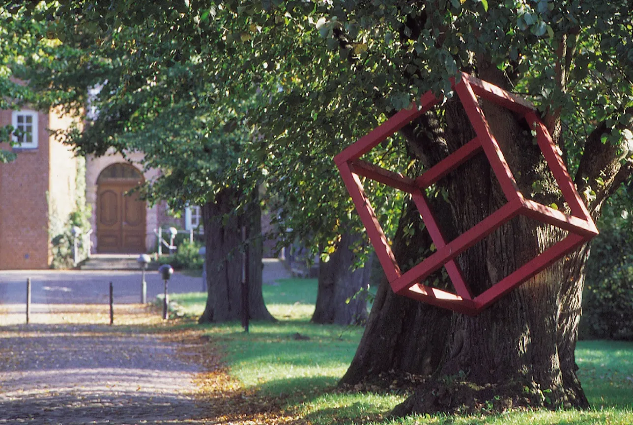Ein großer roter Kubus aus Aluminium hängt in der Linde vor dem Schloss.