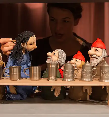 Im Vordergrund Handpuppen: Schneewittchen und die sieben Zwerge, die Spielerin im Hintergrund.