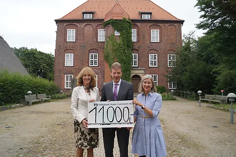Rosemarie Meyer, Henning Porth und Bettina Roggmann halten gemeinsam einen übergroßen Scheck. Im Hintergrund sieht man das Schloss. 