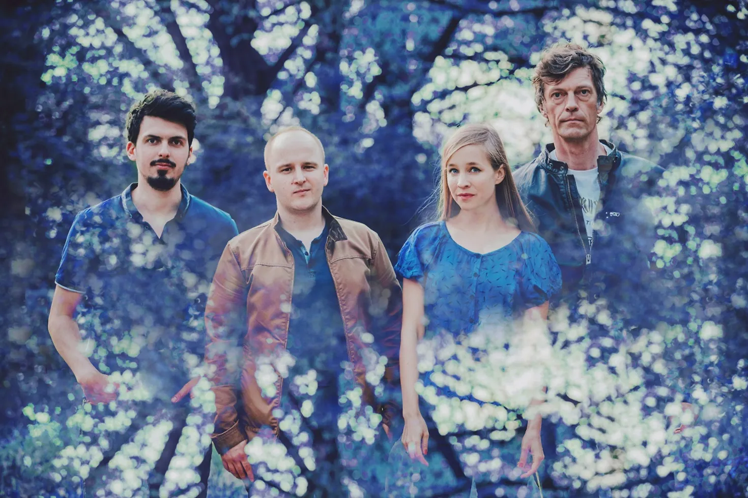 Ein Bild der vier Musiker, drei Männer und eine Frau, mit blauen Effekten im Vorder- und Hintergrund.